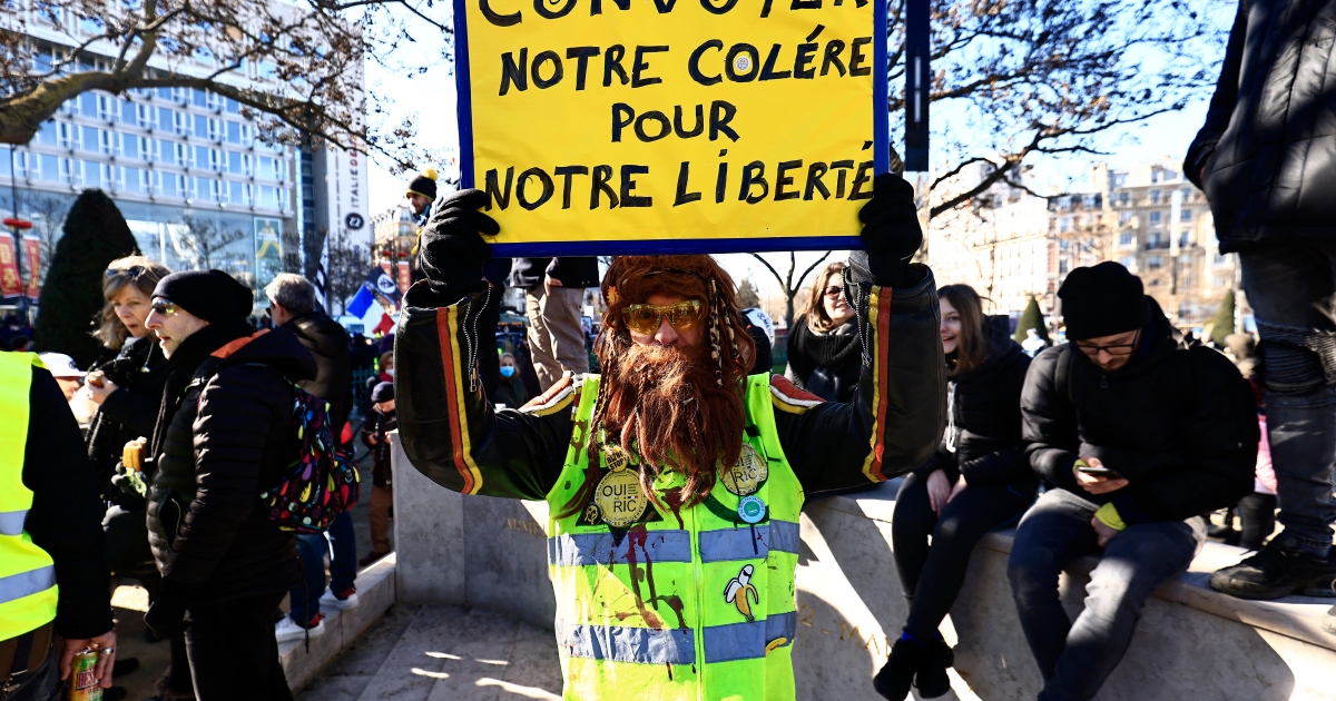 A demonstrator wearing a yellow vest holds a sign reading "Let's convoy our anger for our liberty"